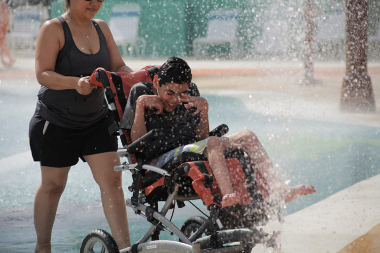 Young man in wheelchair reacts to the water splashing on him while on an amusement park ride. 